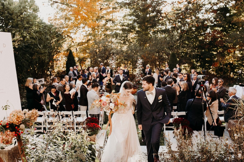 Bride and groom walk up the aisle at a fall outdoor ceremony with full-service wedding planning.
