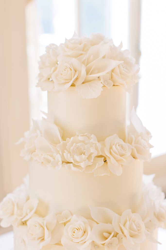 Three-tiered white wedding cake adorned with delicate sugar flowers, designed as part of the couple’s wedding weekend itinerary to reflect their personal style and celebration details