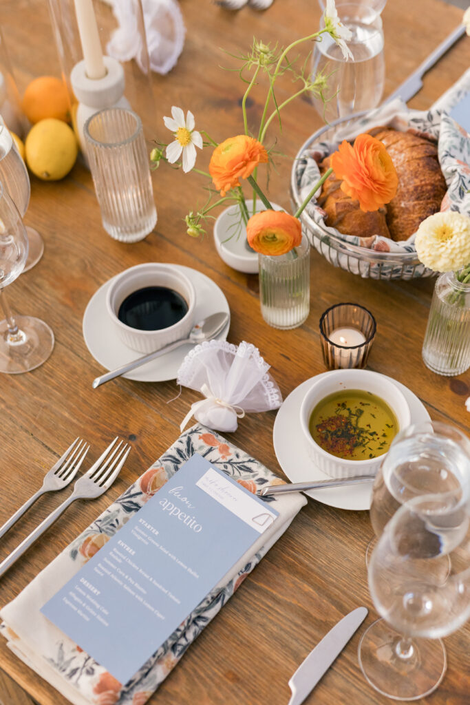 Elegant breakfast table setting with fresh bread, olive oil, coffee, florals, and a candlelit ambiance.