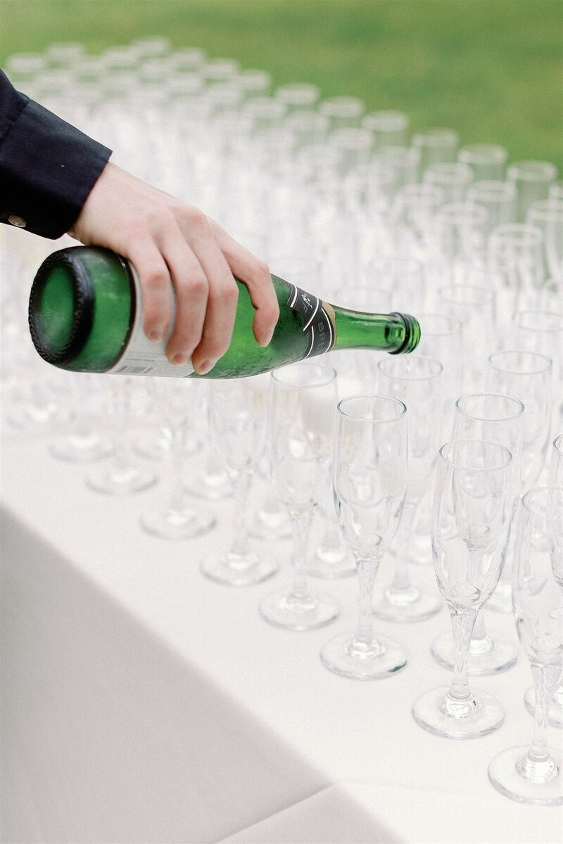 person pouring champagne into champagne flutes lined on a white table cloth | destination wedding in italy