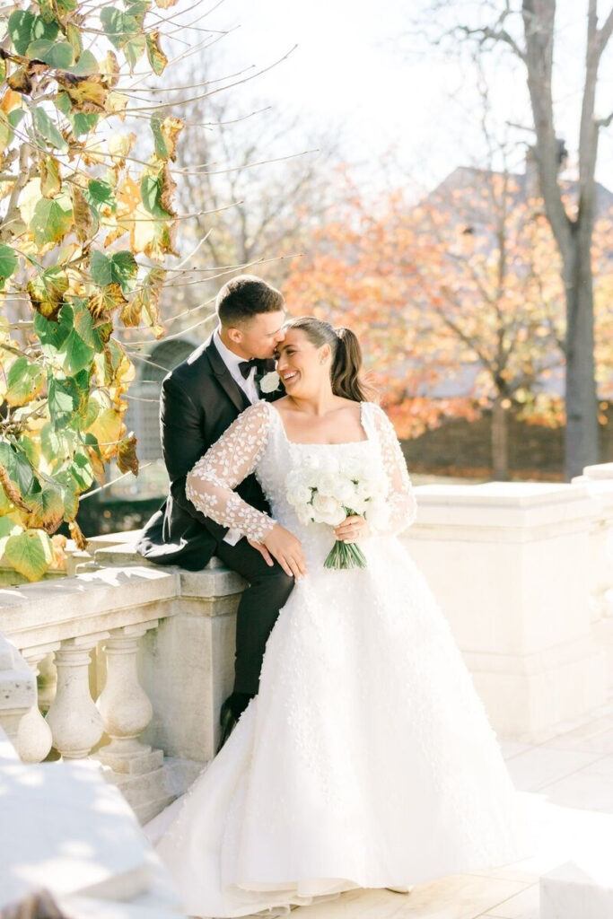 Joyful bride and groom embrace on sunlit terrace surrounded by foliage—ideal for fall weddings in New England.