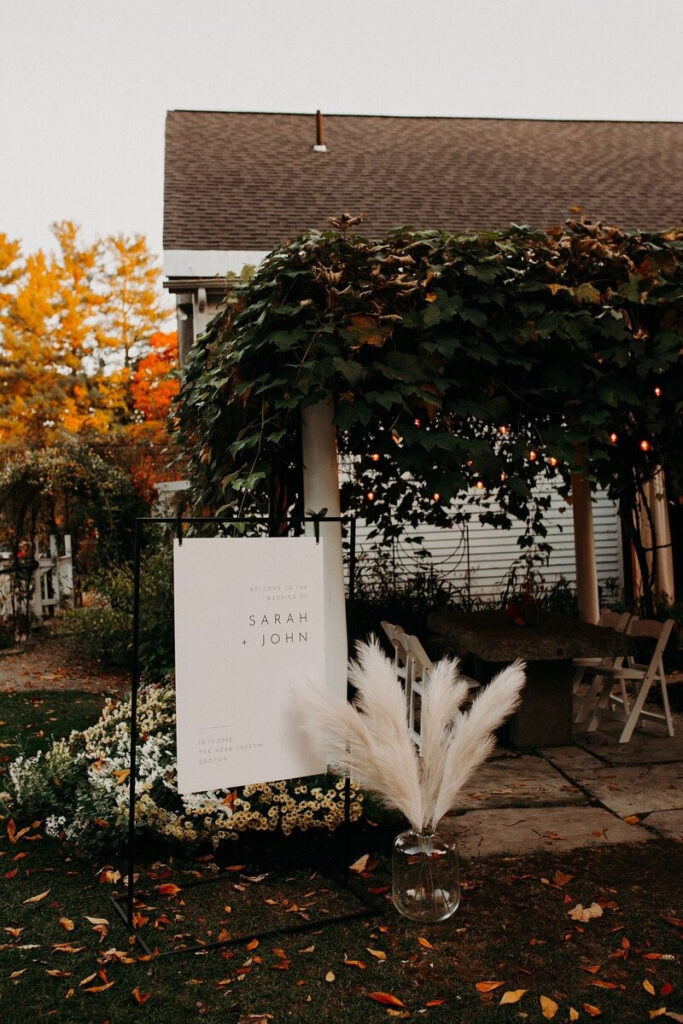 Vine-covered pergola with glowing lights and autumn trees, capturing cozy charm of fall weddings in New England.