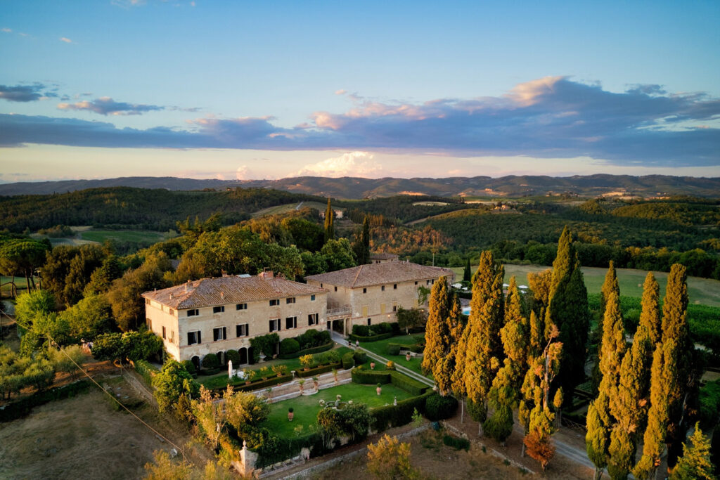 Historic stone villa in Tuscany surrounded by cypress trees and rolling hills at sunset, one of the most picturesque villas in Italy.