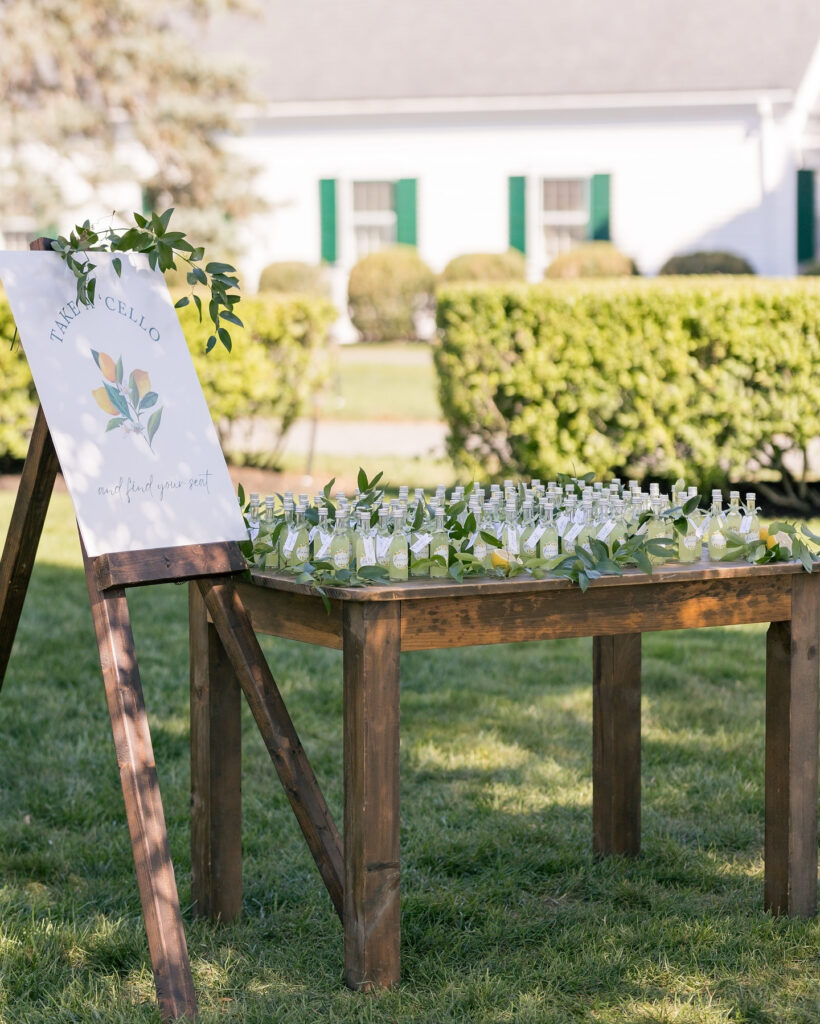 Outdoor wedding display with limoncello escort cards on a rustic wooden table and greenery accents.