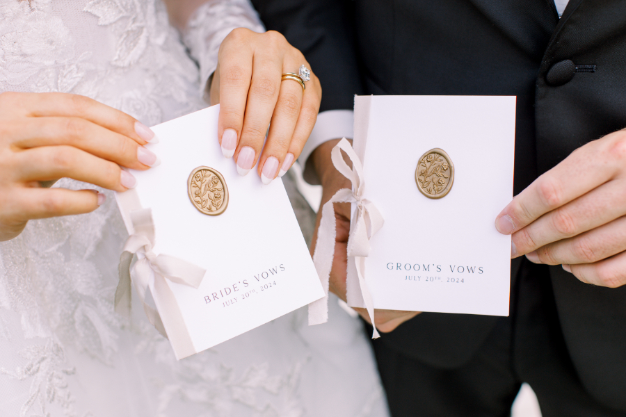 Close-up of bride and groom holding personalized vow booklets tied with ribbon and sealed with wax.