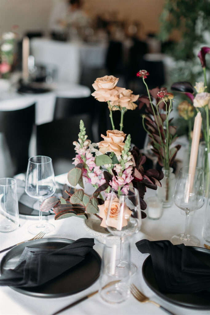 Modern tablescape featuring black plates, black napkins, neutral florals, and blush taper candles.