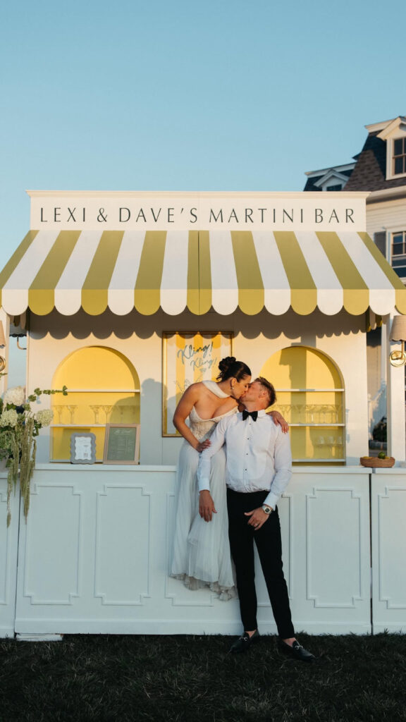 Couple kissing in front of custom martini bar during their full-service wedding weekend celebration.