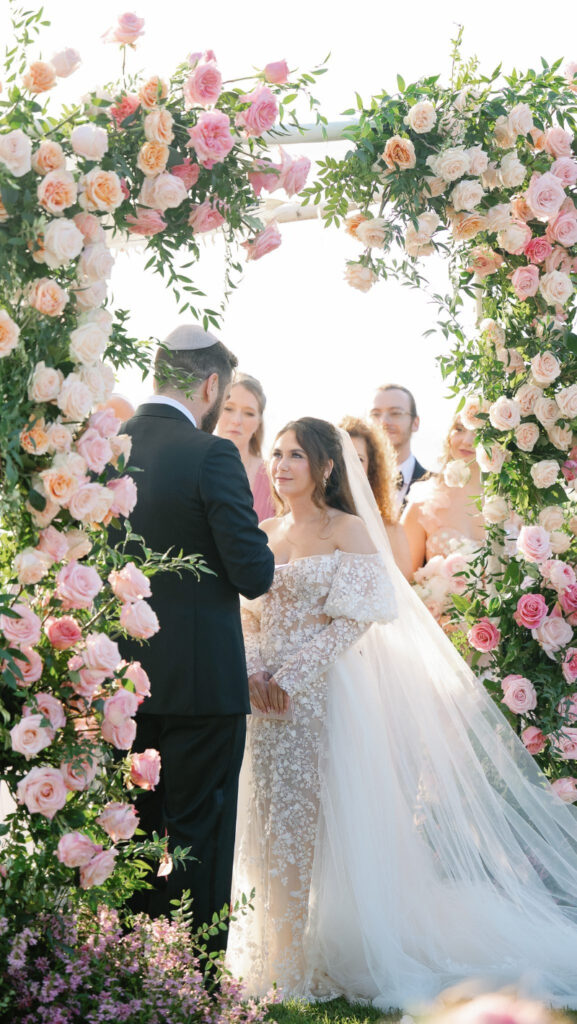 Bride and groom exchanging vows under floral arch during their full-service wedding weekend ceremony.