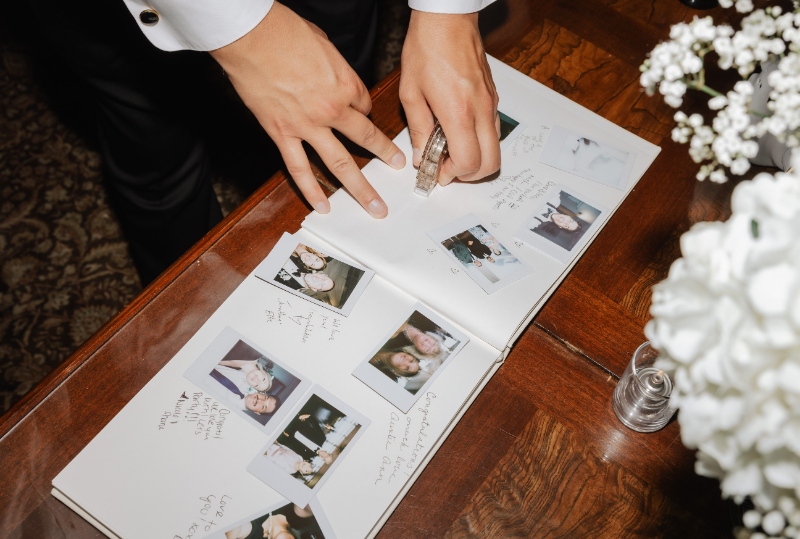 Guestbook with Polaroid photos and handwritten messages, as a guest adds a photo using clear tape.
