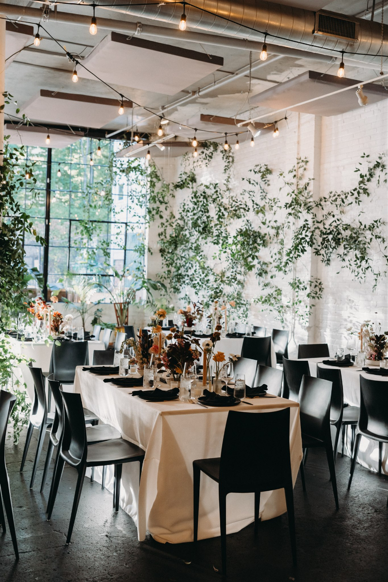 Modern indoor reception with sculptural florals and black chairs, reflecting 2026 wedding design trends.