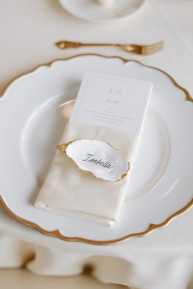 Elegant place setting with gold-trimmed oyster shell escort card at one of the best intimate wedding venues.