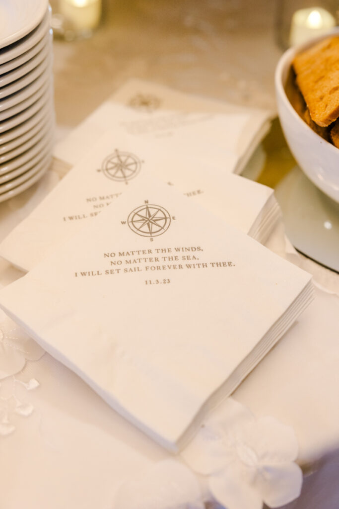 Custom cocktail napkins with nautical quote and compass design as part of personalized wedding details.