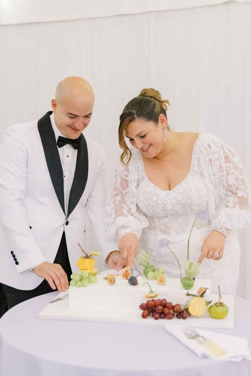 Bride and groom cutting modern rectangular wedding cake topped with fresh fruit.