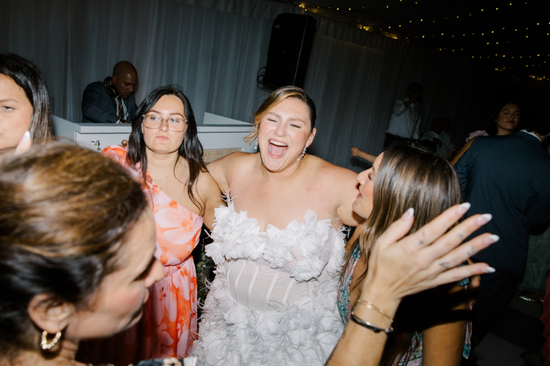 Bride laughing with friends on crowded dance floor during reception at a Blithewold Mansion wedding