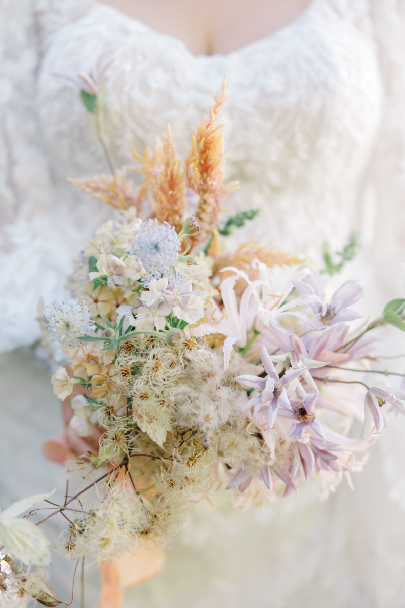 Bride holding textured pastel bouquet with soft lilac and peach blooms.