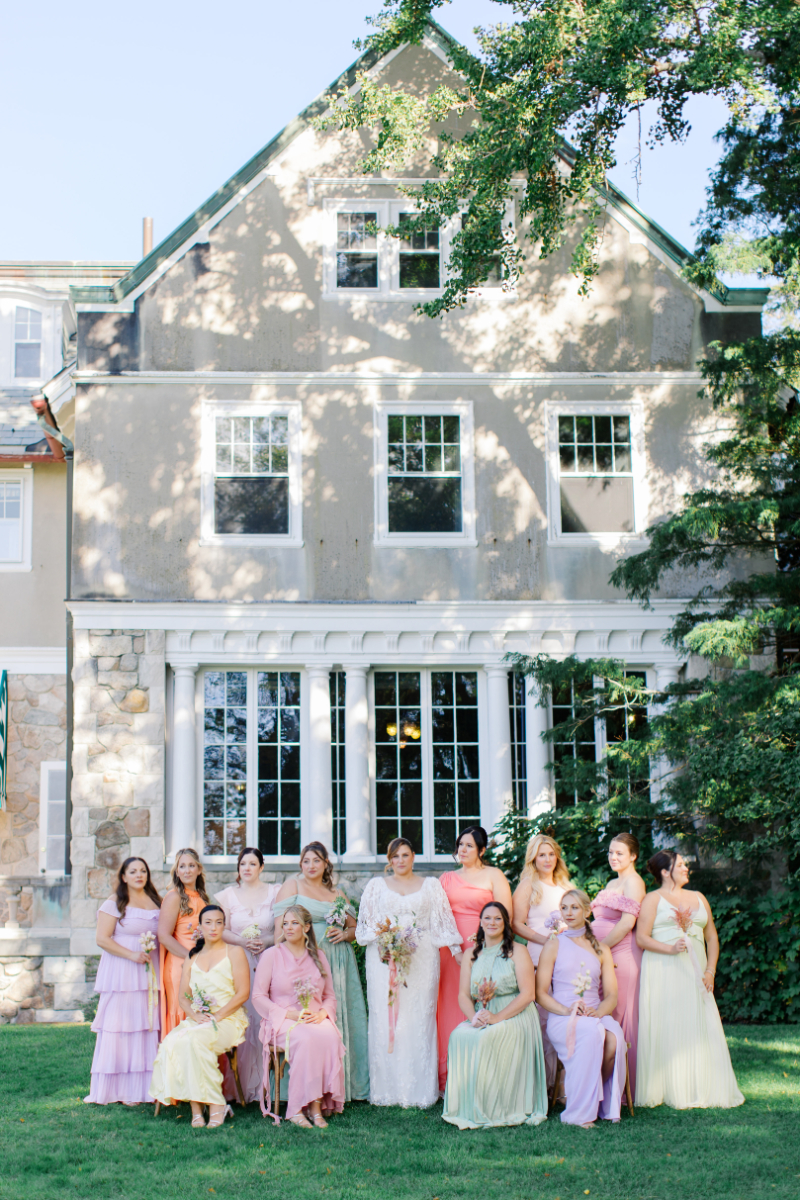 Bridal party in pastel dresses posing in front of historic estate.