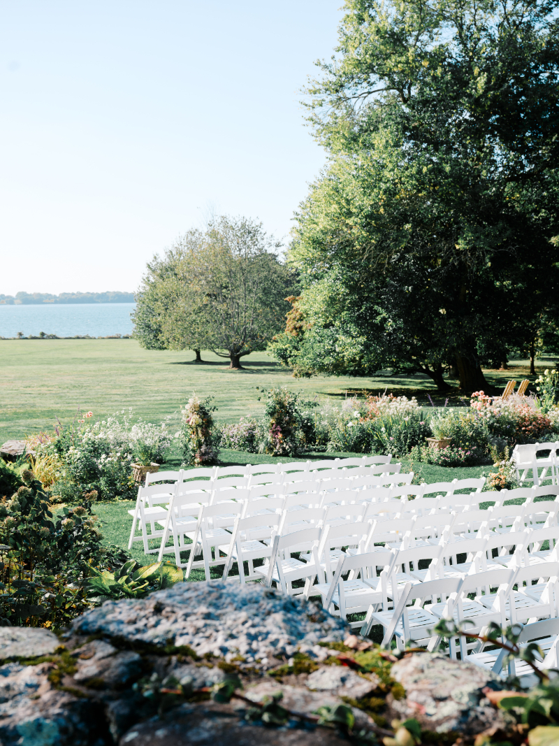 Garden ceremony setup with white chairs overlooking lawn and waterfront views.