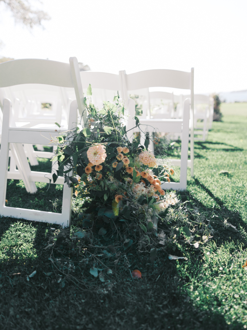 White ceremony chairs lined with peach and green floral aisle arrangements.