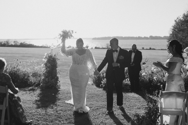 Bride and groom celebrating down the aisle after outdoor waterfront ceremony.