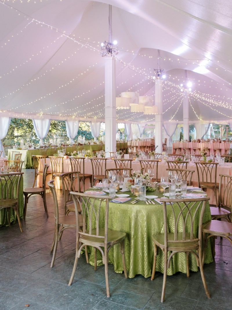 Round reception tables with green linens and wood chairs under string lights.
