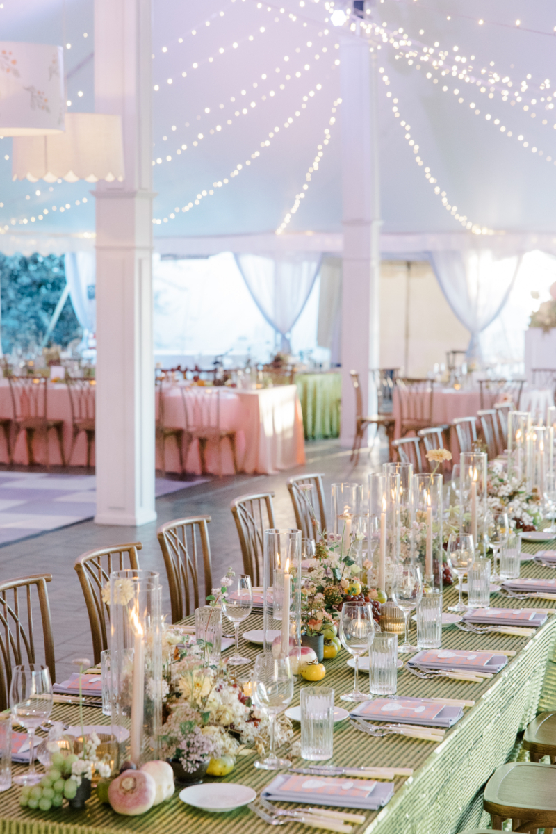 Reception tent interior with long tables, candles, and string lights overhead.
