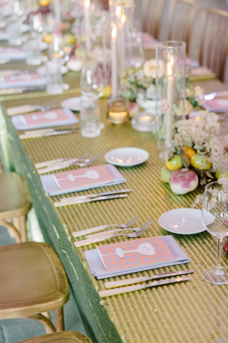 Reception table with green textured linen, patterned menus, candles, and fruit accents.