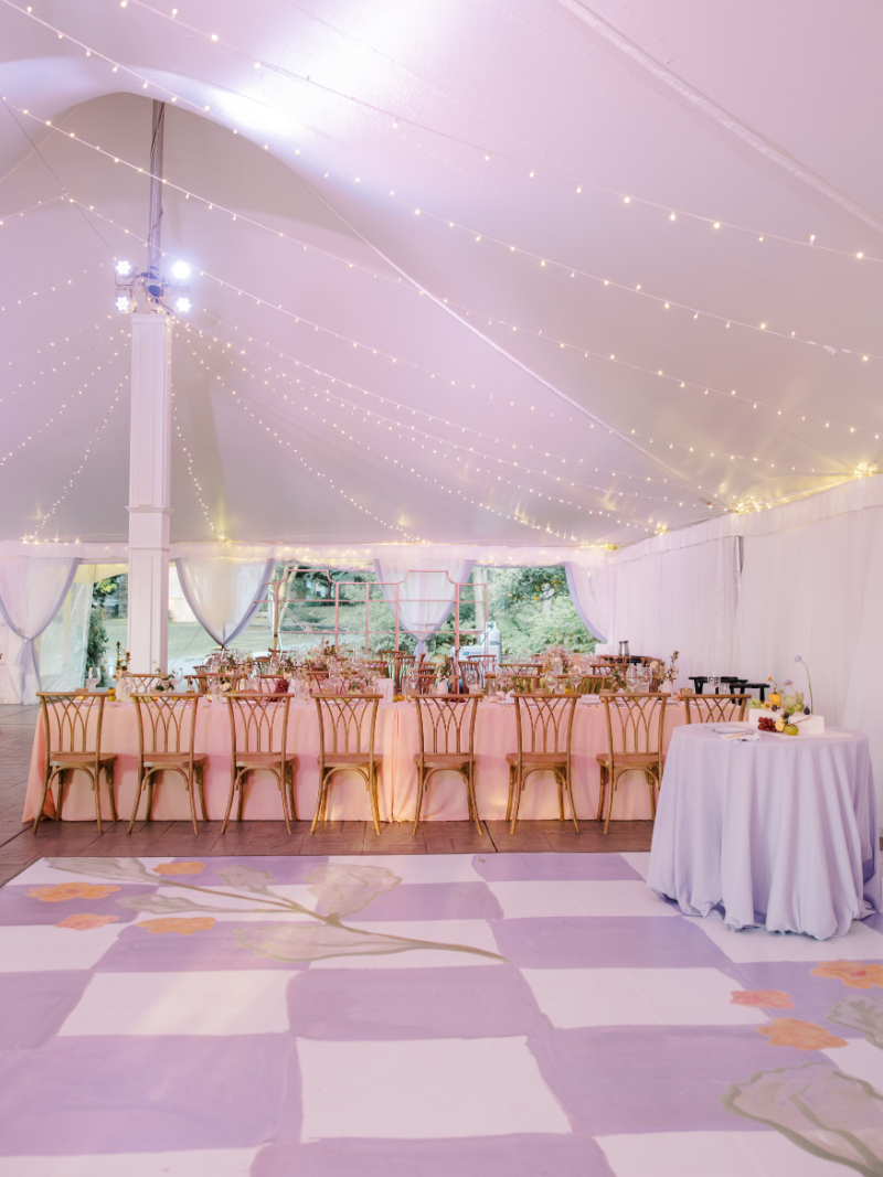 Reception tent with pastel dance floor, long tables, and string lights overhead.