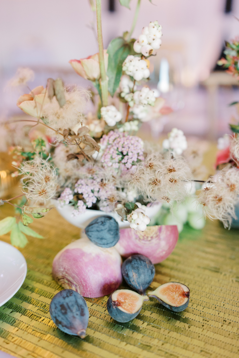 Floral centerpiece with figs, pomegranates, and soft pastel blooms on green linen.