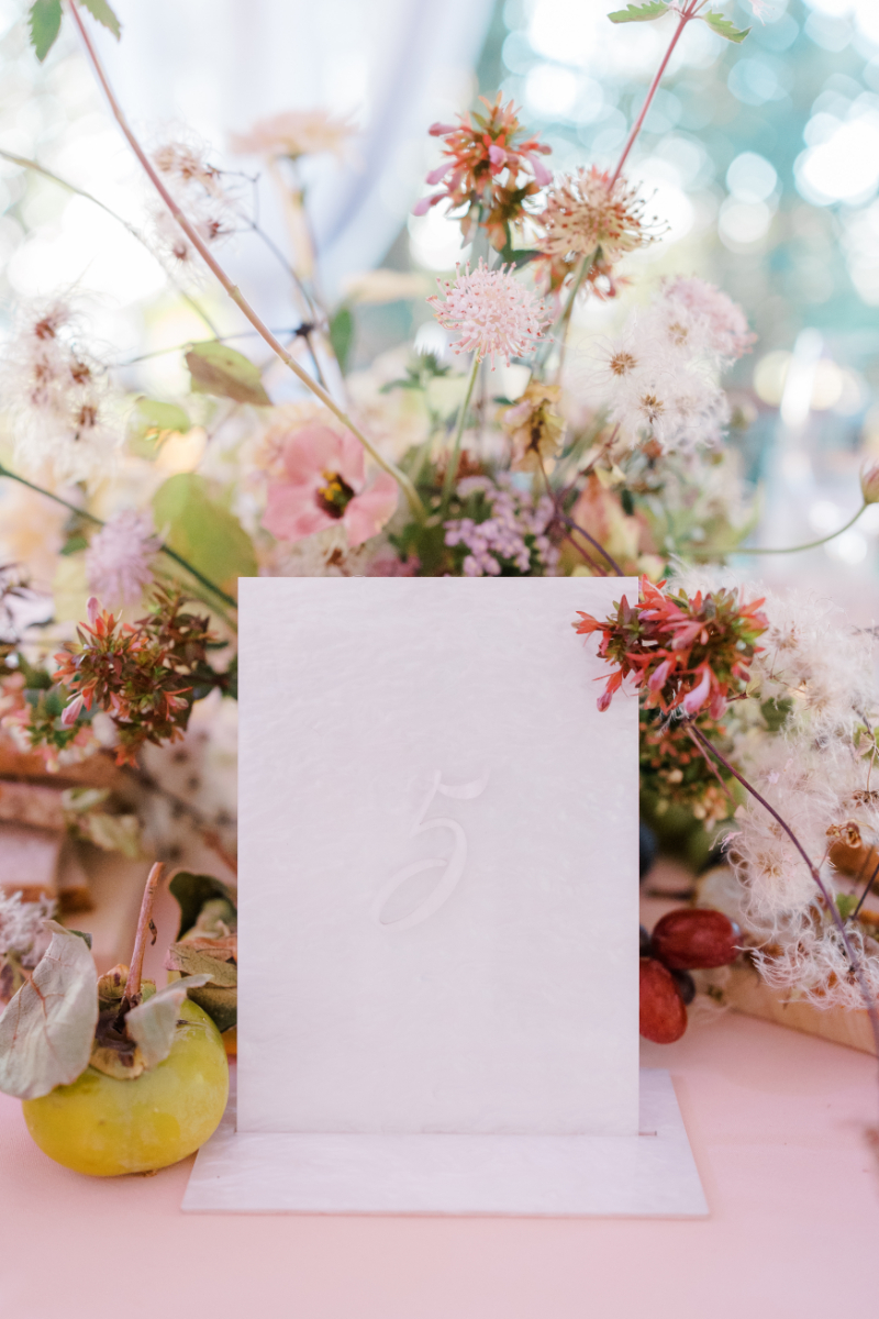 Floral arrangement with pastel blooms and table number card on pink surface.