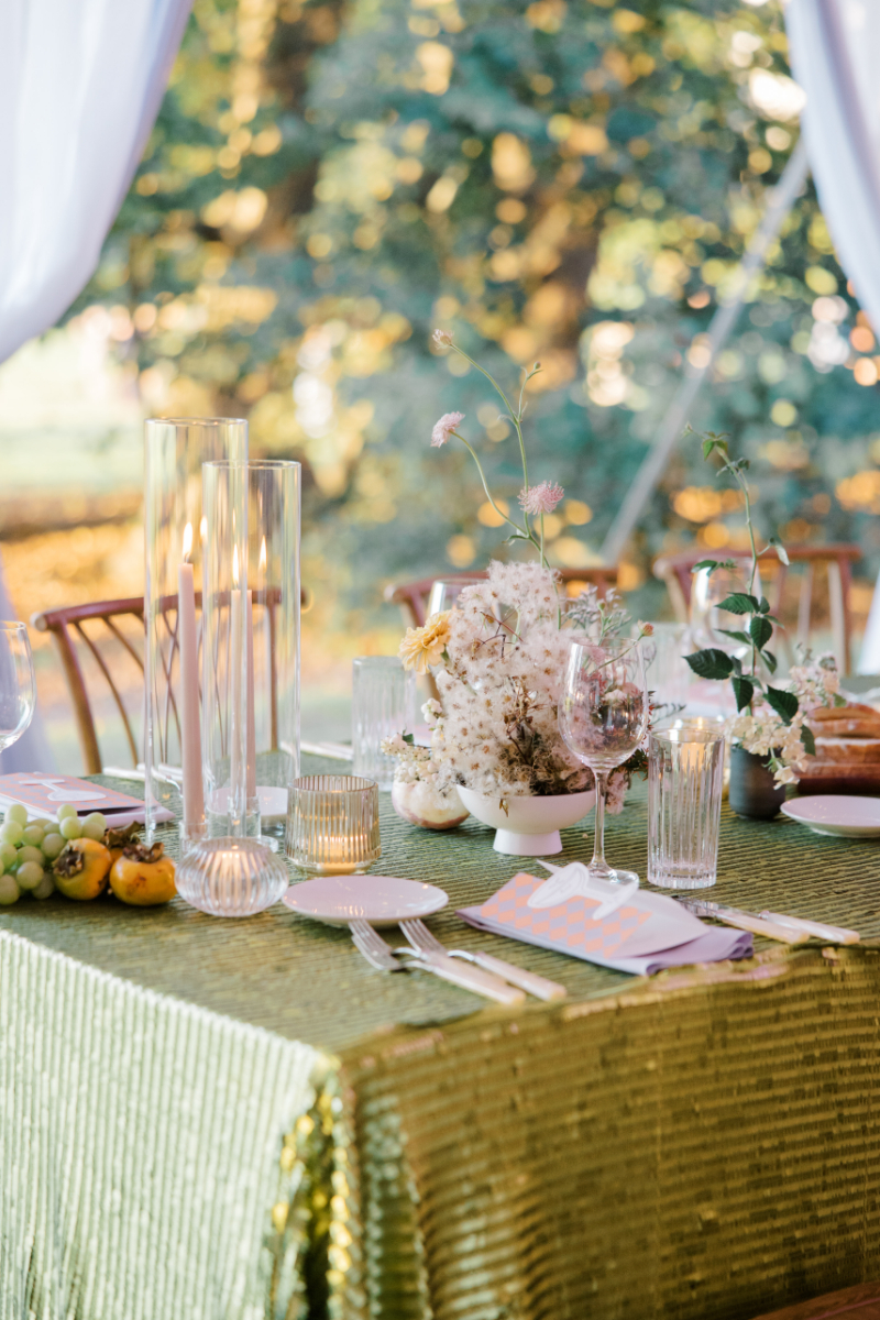 Reception table with green sequin linen, candles, fruit, and soft floral centerpiece.