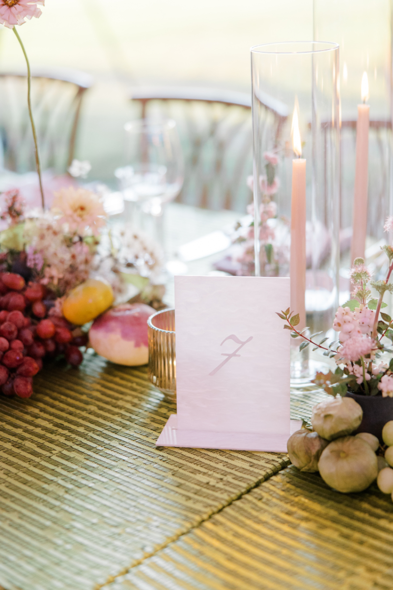 Green textured table with pink candles, fruit accents, and table number card.