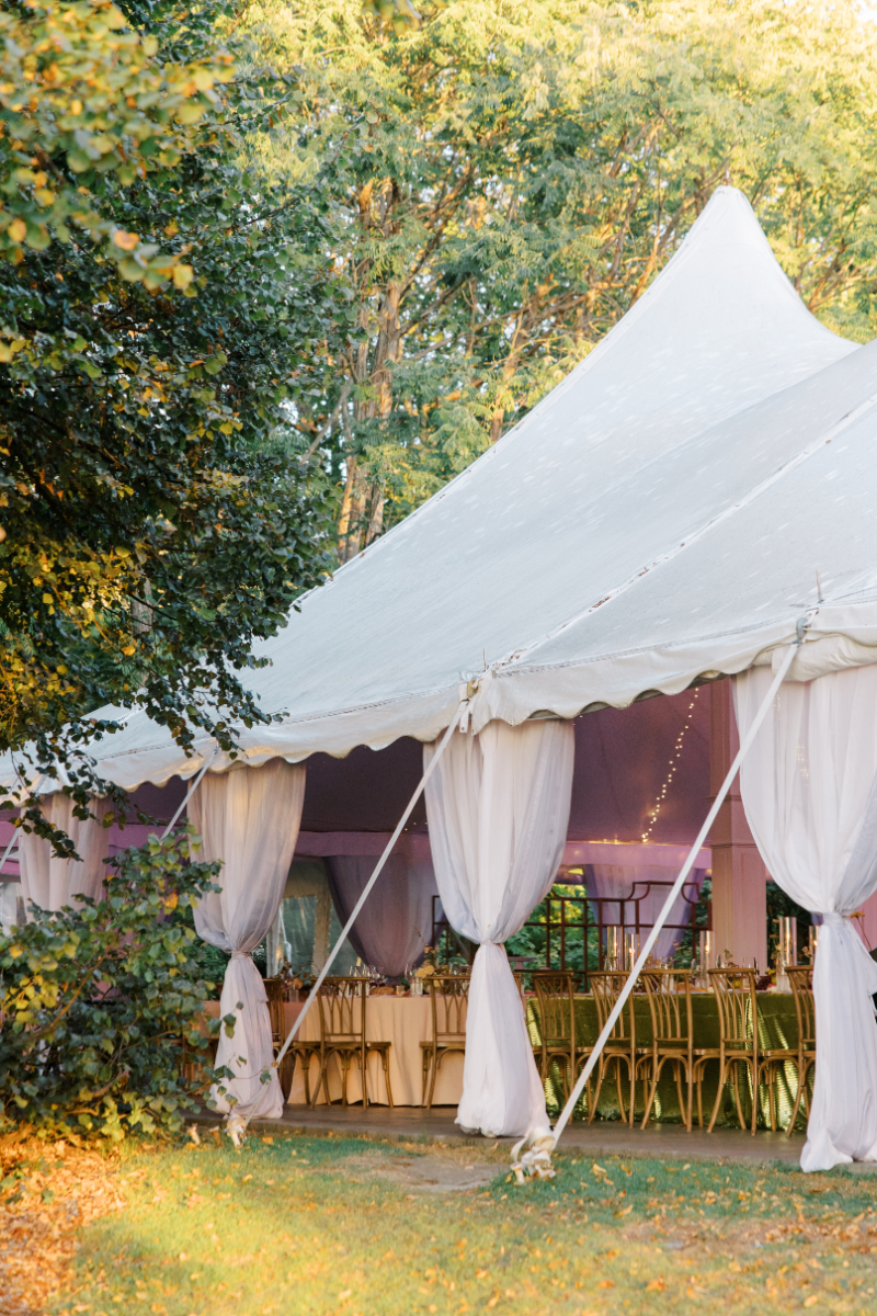 White reception tent set on lawn with draped fabric and warm evening light.