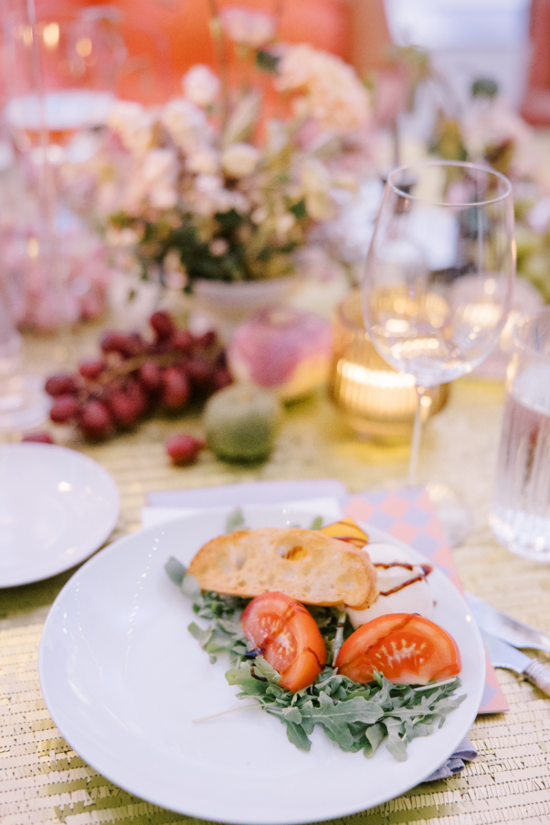 Plated salad with tomatoes and greens on candlelit reception table.