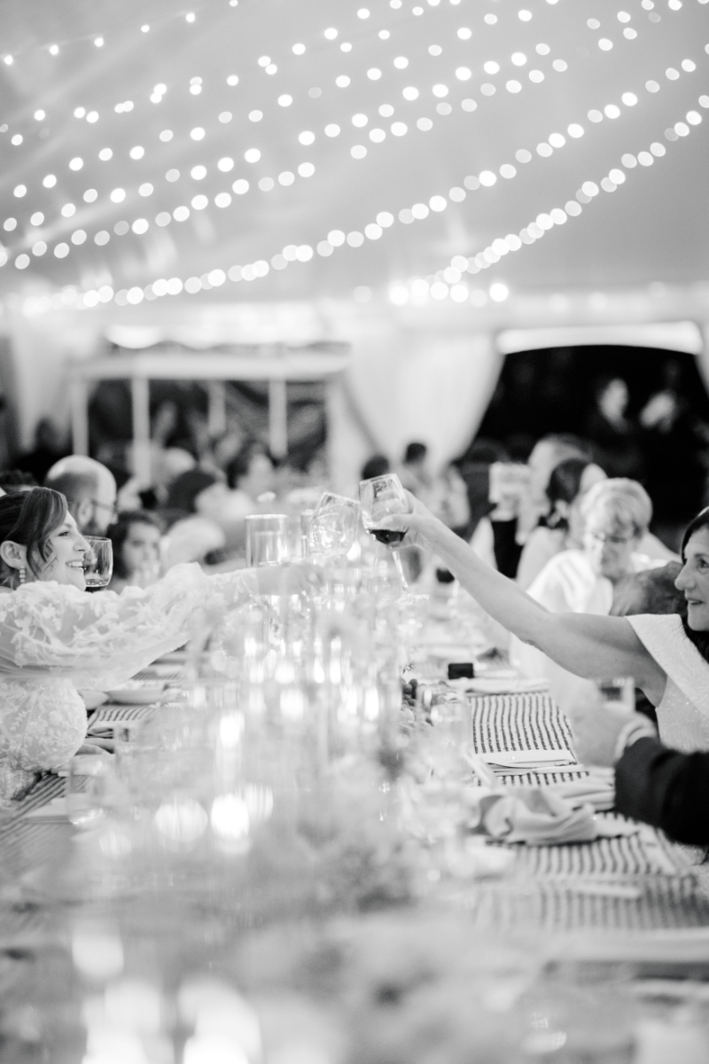 Guests toasting at long candlelit reception table under string lights.