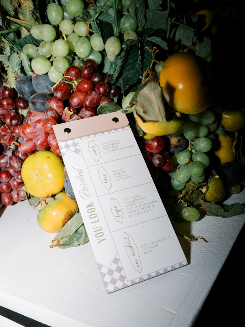 Seating chart card displayed against lush fruit and greenery arrangement.