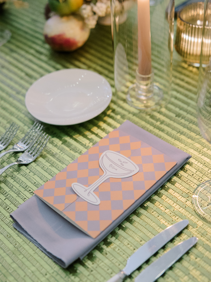 Green textured tablescape with patterned menu, candles, and fruit accents.