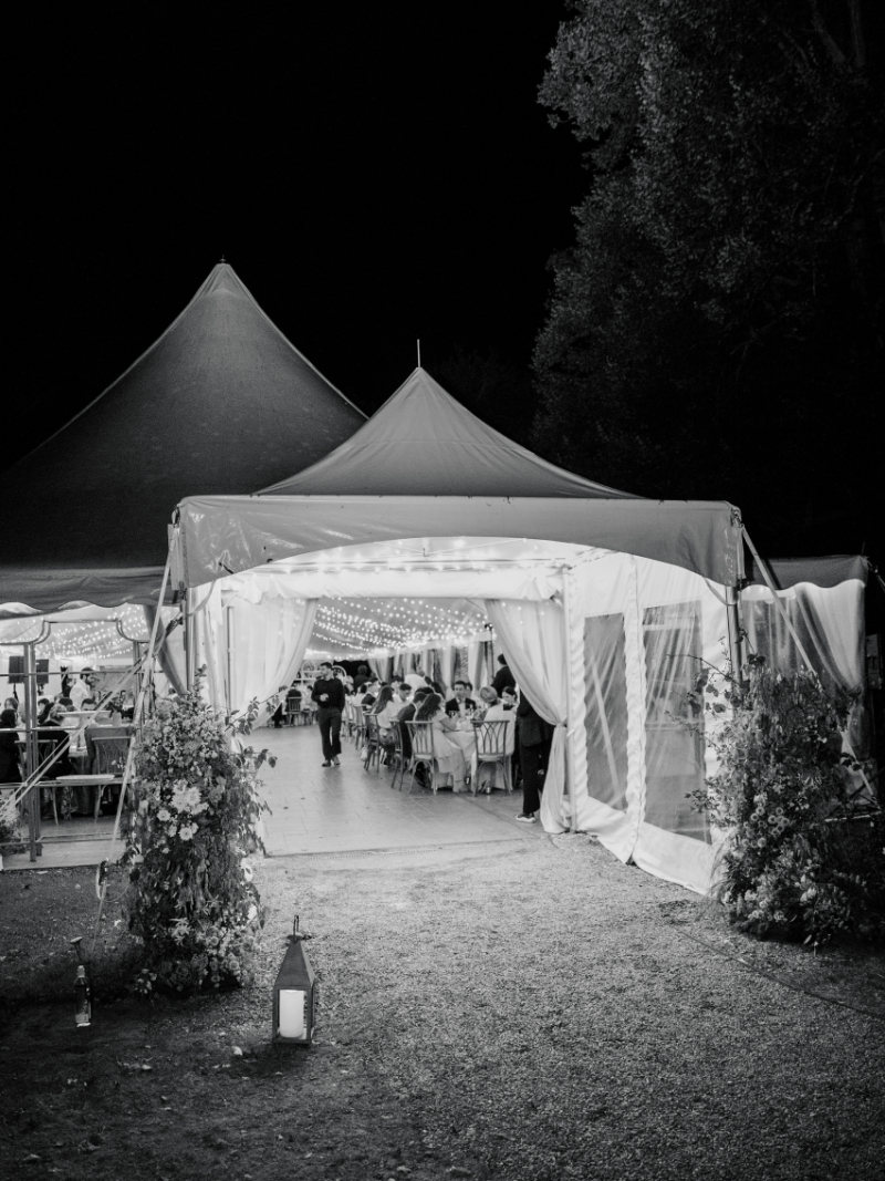 Reception tent at night with glowing string lights and guests inside.