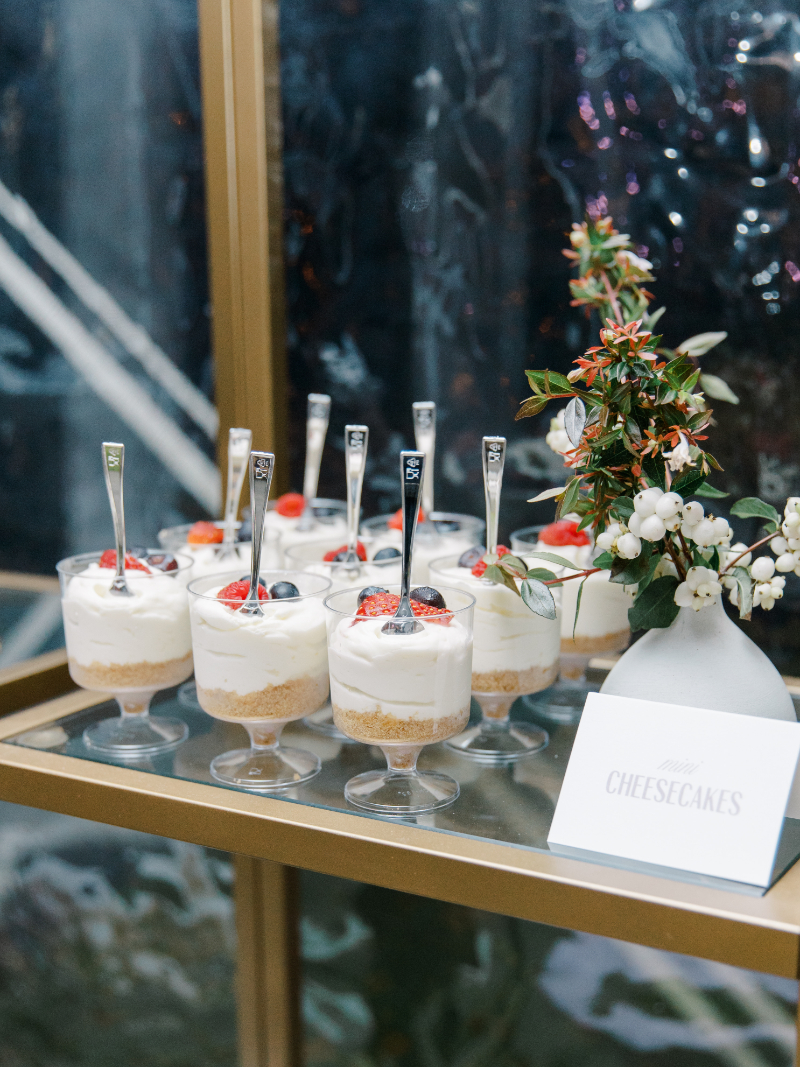 Mini cheesecakes in glass cups displayed with floral detail and sign.