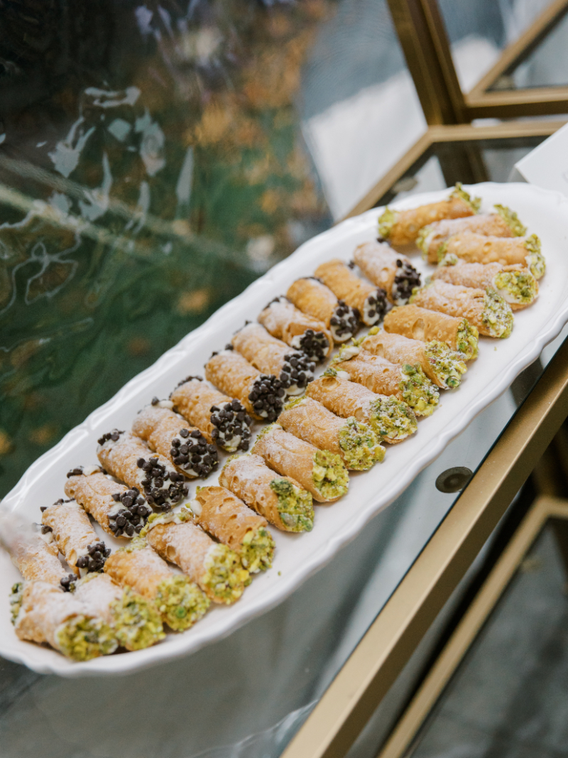 Tray of Italian pastries and cannoli arranged on white dessert platter.