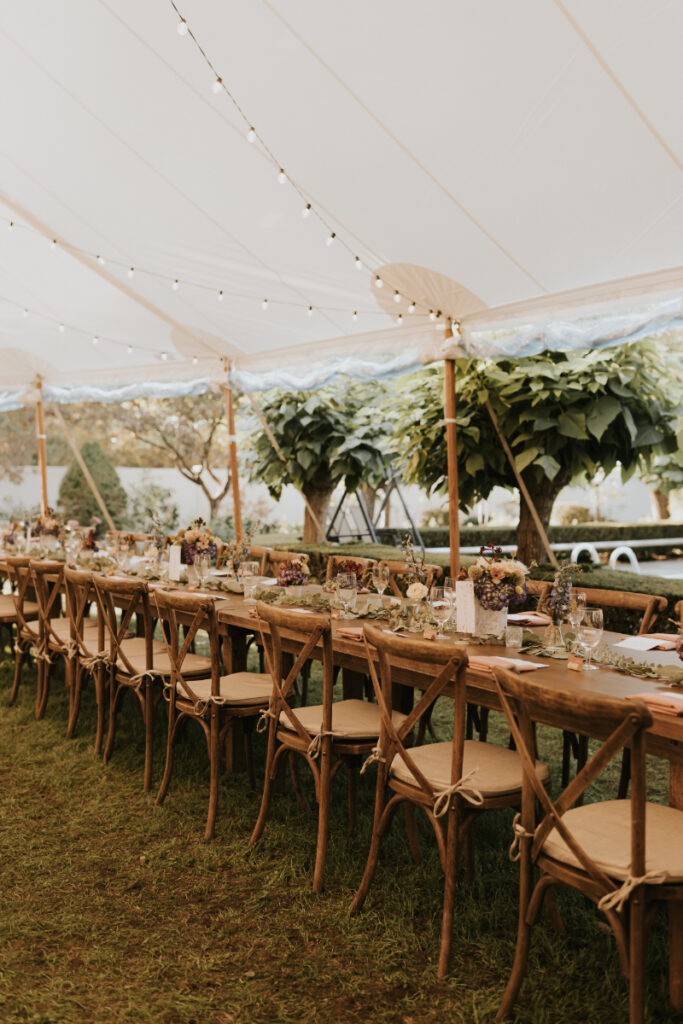 Long banquet tables inside sailcloth tent at a wedding.