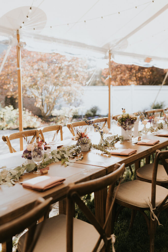 Long wooden reception table with florals at Italian countryside wedding under tent.
