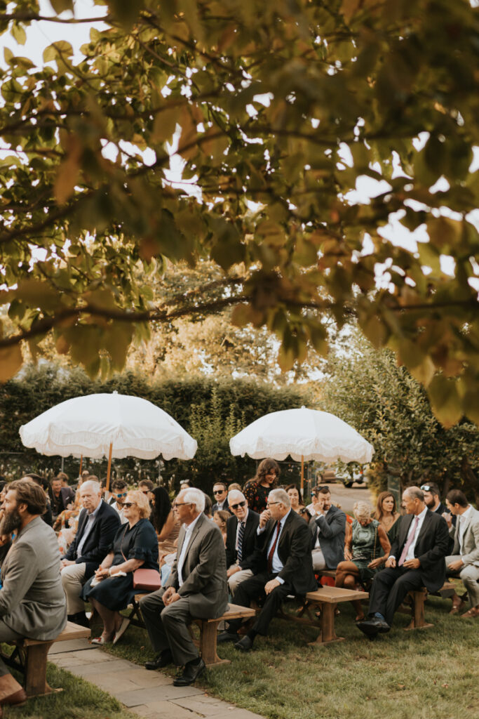 Guests seated under umbrellas during a wedding ceremony.