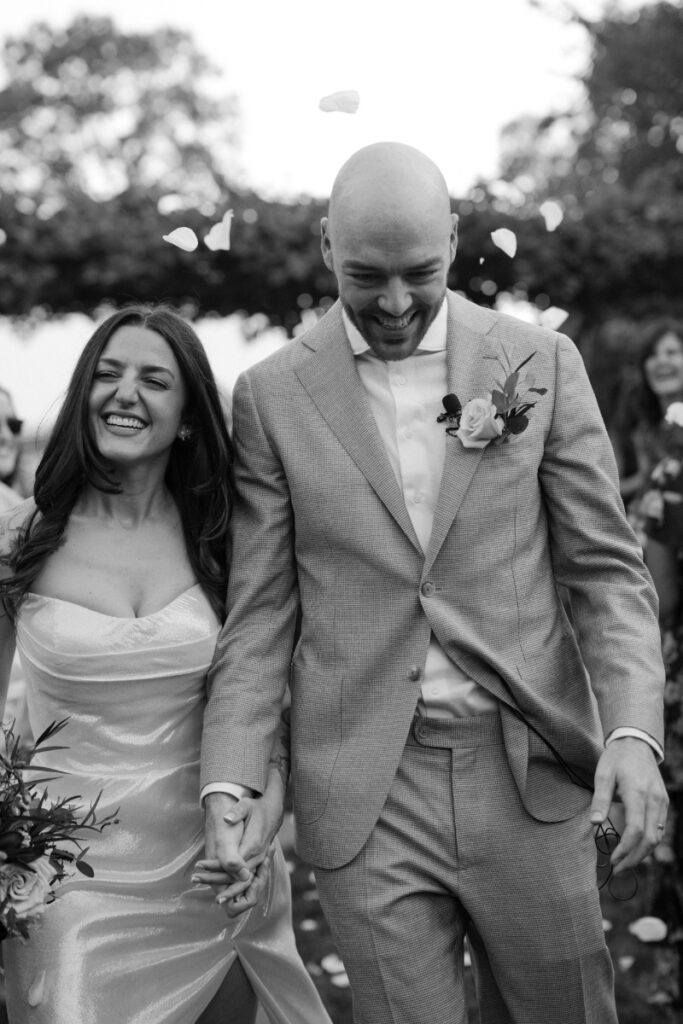 Bride and groom smiling under grape vines during Italian countryside wedding ceremony.