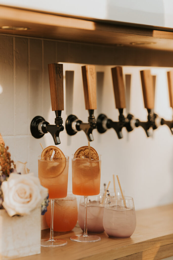 Cocktail taps and signature drinks at Italian countryside wedding reception bar.