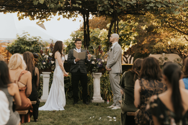 Couple standing under grape vines during Italian countryside wedding ceremony.