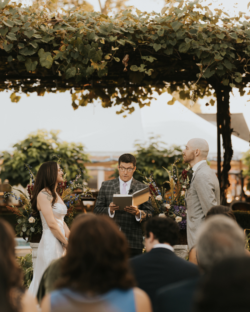 Couple exchanging vows under grape vines at Italian countryside wedding ceremony.