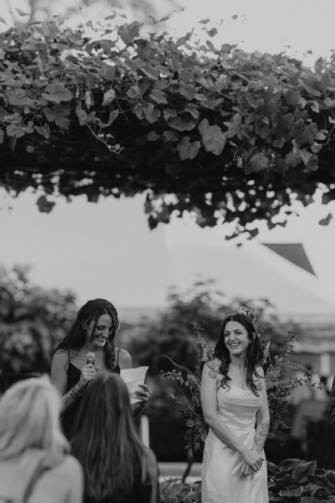 Bride laughing beneath grape vines at Italian countryside wedding ceremony.