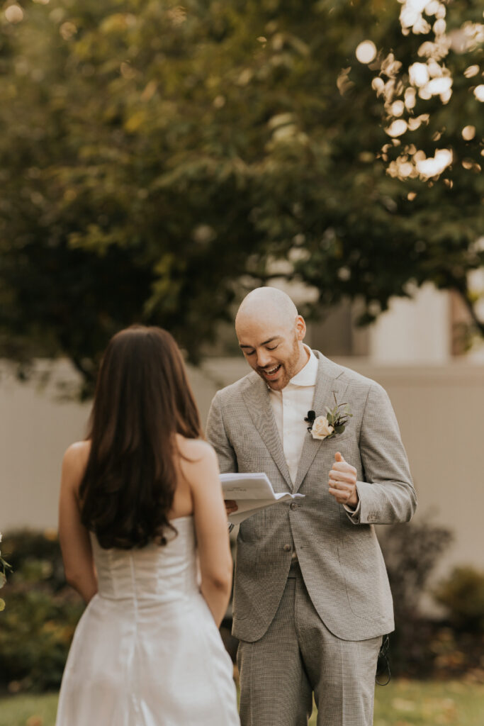 Groom smiling while reading vows at Italian countryside wedding ceremony.