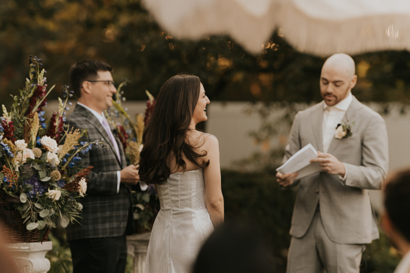 Bride smiling during Italian countryside wedding vows under garden trees.
