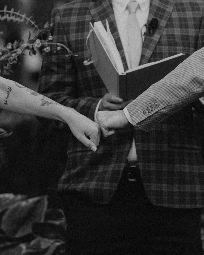 Couple holding hands during Italian countryside wedding ceremony under grape vines.